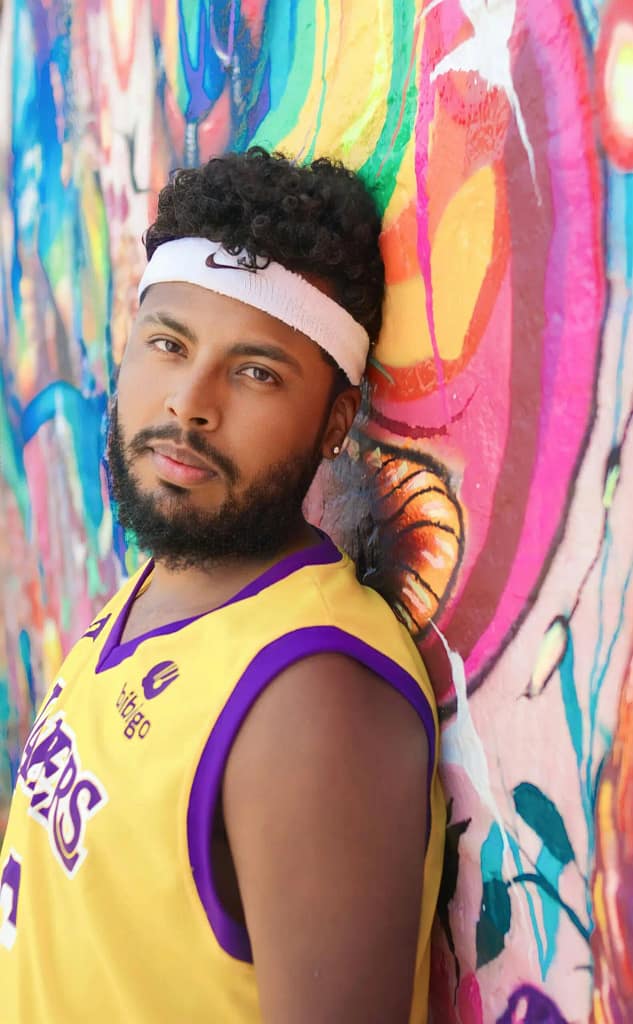 Portrait of a young man in sportswear leaning against a vibrant graffiti wall, showcasing urban culture.